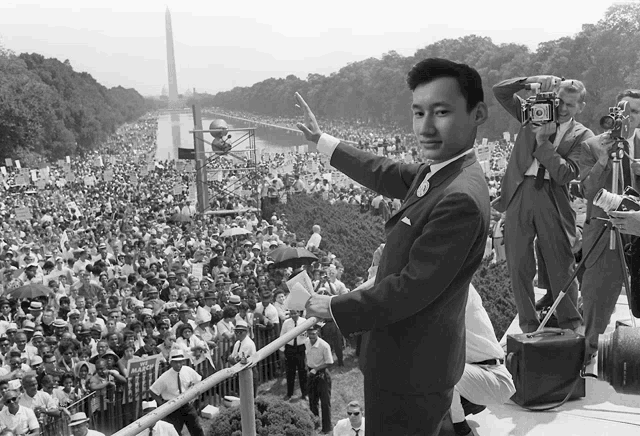 a man in a suit stands in front of a large crowd