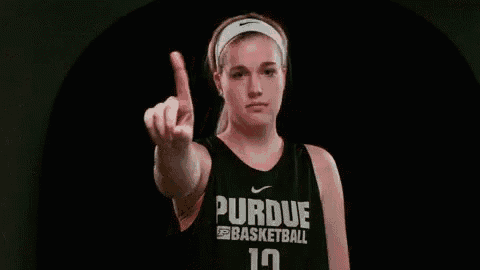 a young woman in a purdue basketball jersey is pointing her finger at the camera .
