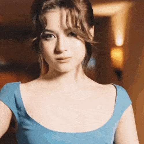 a woman in a blue dress is looking at the camera and making a funny face .