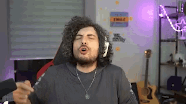 a man with curly hair is wearing headphones and a necklace and is making a funny face .