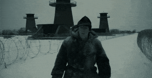 a man in a fur coat stands in the snow in front of barbed wire