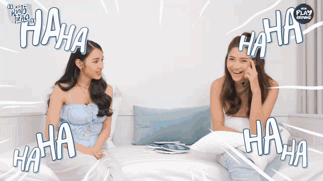 two women are sitting on a bed and laughing with the play review written on the bottom right