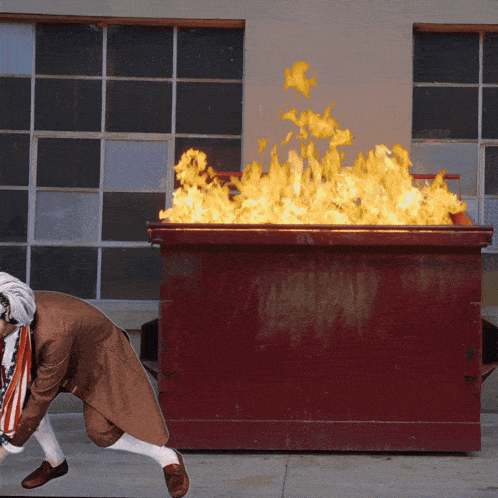 a red dumpster is on fire and a man is running towards it