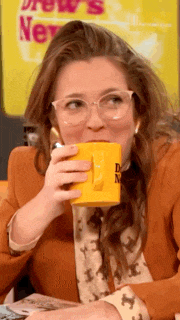 a woman with glasses is drinking from a yellow mug