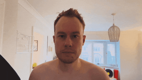 a man without a shirt looks at the camera with his hand on his head