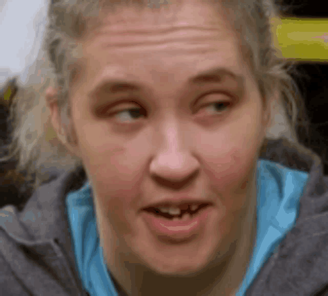 a close up of a woman 's face with a gray hoodie on and a blue shirt .