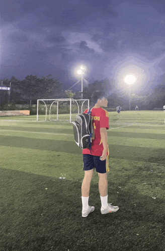 a man standing on a soccer field with a backpack and a red shirt that says v390