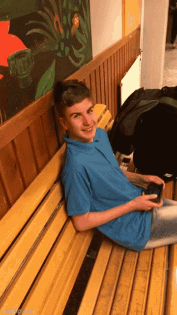 a young man in a blue shirt is sitting on a wooden bench