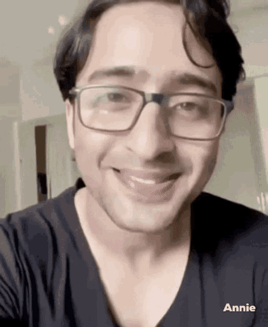a man wearing glasses and a black shirt is smiling and looking at the camera .