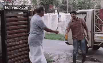 two men are shaking hands in front of a truck in a movie .