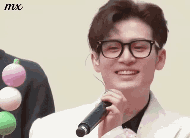 a man wearing glasses is smiling while holding a microphone