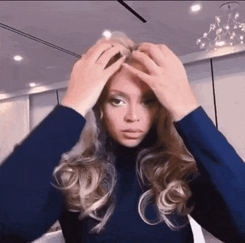 a woman in a blue turtleneck is putting her hair in a ponytail .