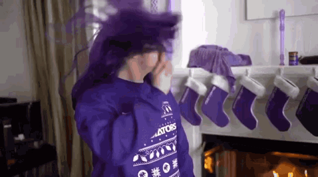 a person in a purple sweater is standing in front of a fireplace .