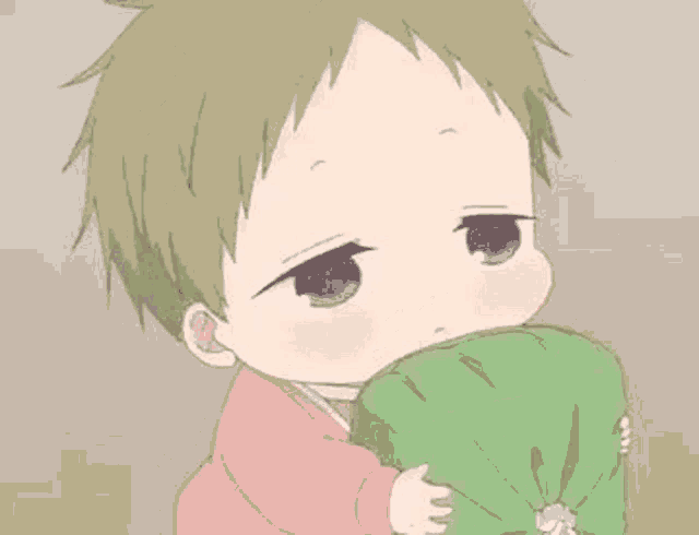a baby is holding a green pillow in his hands and looking at the camera .