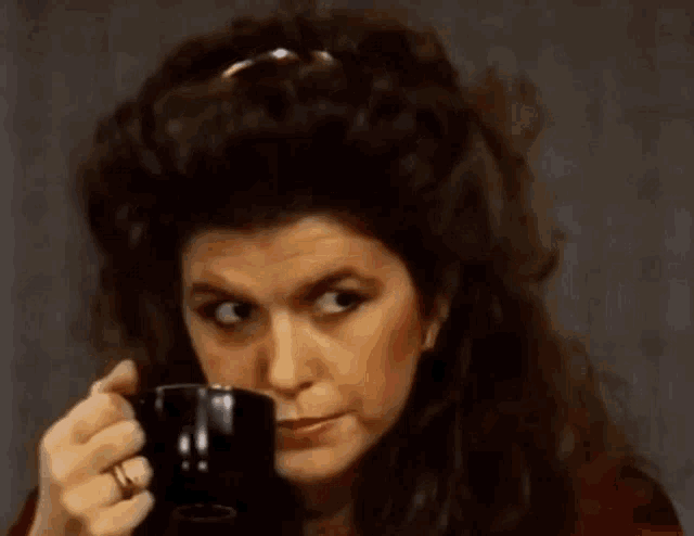 a woman is drinking from a black mug with a ring on her finger .