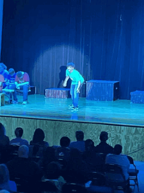 a man on a skateboard stands on a stage in front of an audience