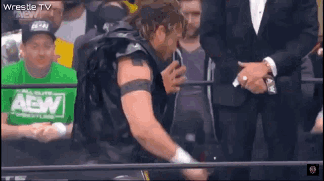 a wrestler wearing a green shirt that says aew is standing in front of a crowd