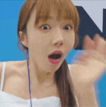 a woman in a white tank top is making a surprised face while waving her hand .