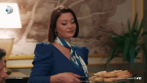 a woman in a blue dress is holding a plate of food in front of a sign that says kanald.com.tr
