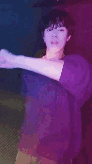 a man in a purple shirt is dancing in a dark room with a purple background .