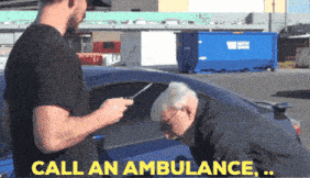 a man in a black shirt is talking to an older man in a blue car while the man says call an ambulance