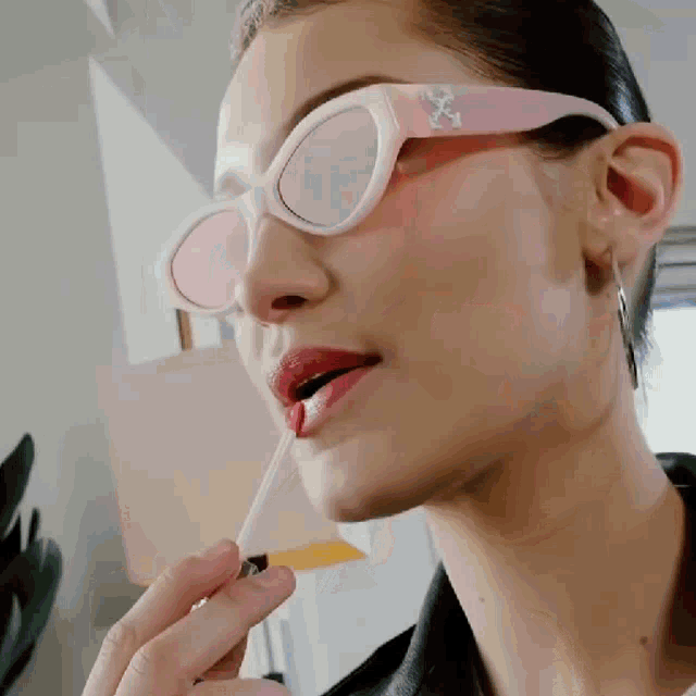a woman wearing sunglasses is applying liquid lipstick to her lips