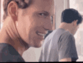 a man is smiling and looking at the camera while another man is standing behind him .