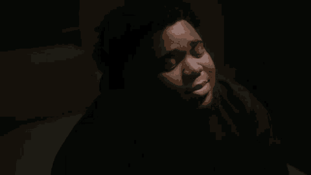 a young man in a black hoodie is sitting in a dark room with his eyes closed .