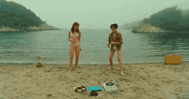 a man and a woman standing on a beach with a record player on the sand
