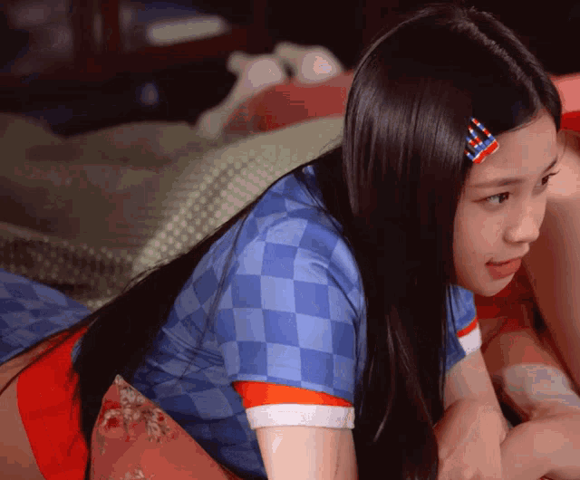 a girl wearing a blue checkered shirt has a red and white hair clip in her hair