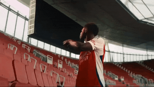 a man in a red and white emirates jersey is standing in a stadium .