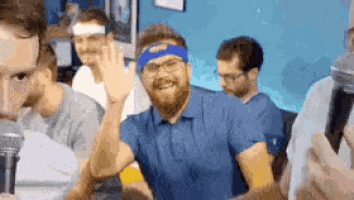 a group of men are sitting around a table with a man wearing a blue headband waving at the camera .