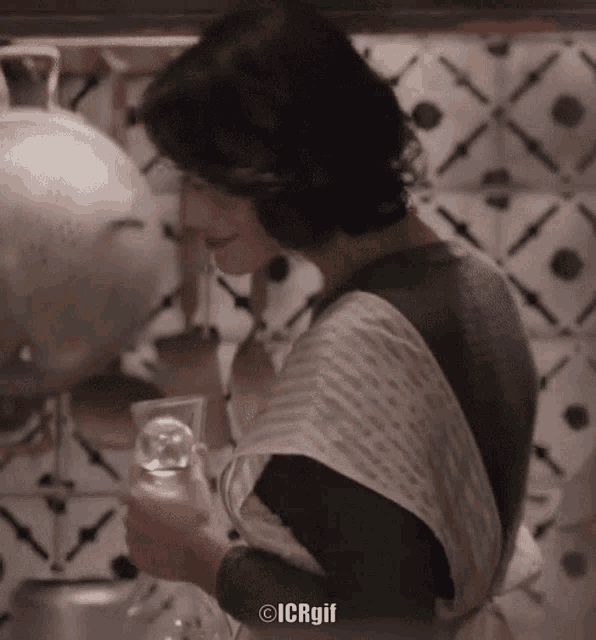 a woman in an apron is holding a glass of water in front of a tiled wall ..