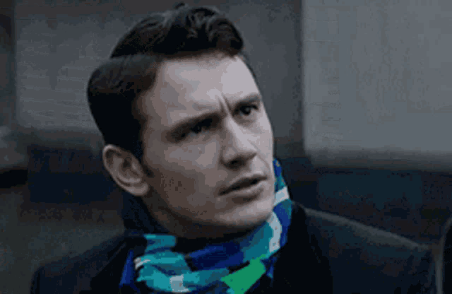 a man wearing a scarf around his neck looks to his left