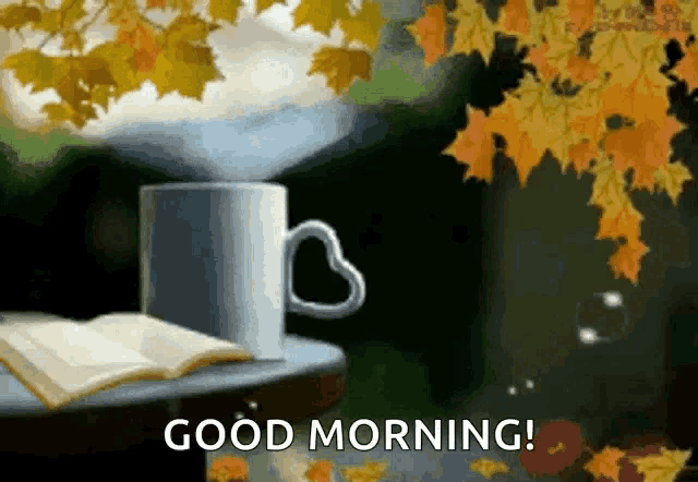 a cup of coffee with a heart shaped handle is on a table with an open book and leaves .