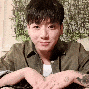 a young man with a tattoo on his arm is sitting on a couch with his hands folded .