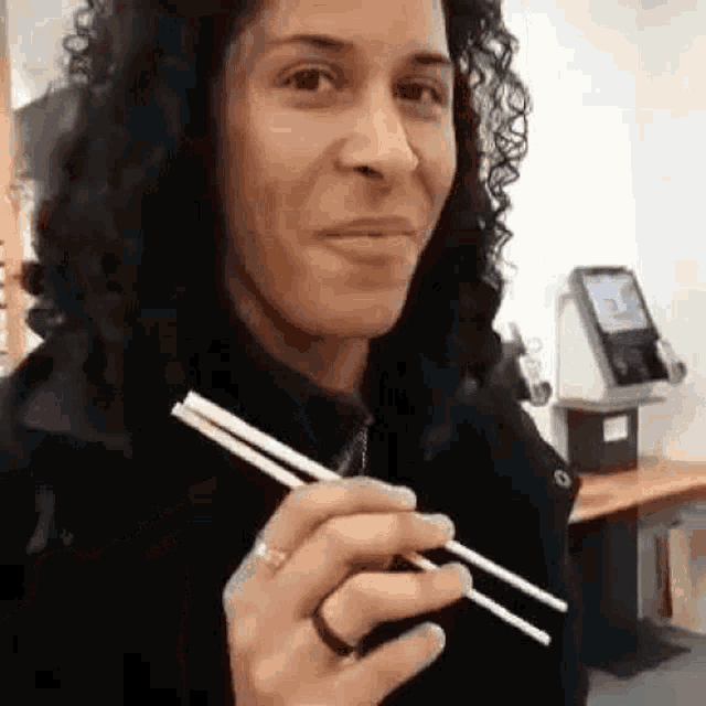 a woman with curly hair is holding a pair of chopsticks in her hand .