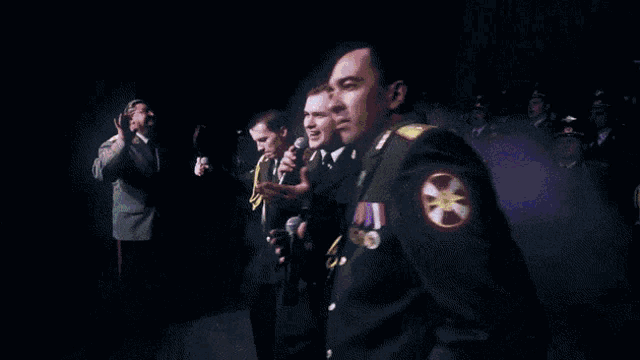 three men in military uniforms singing into microphones on a stage