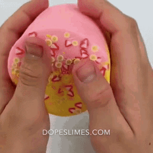 a person is holding a pink and yellow donut with the website dopeslimes.com in the corner