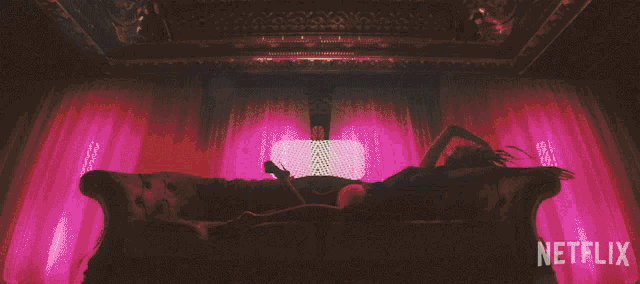 a woman is laying on a couch in front of a window with netflix written on the bottom
