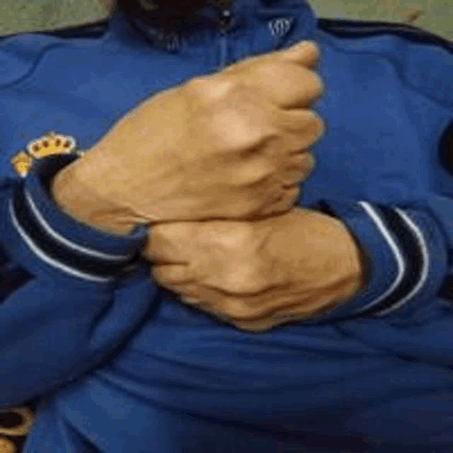 a man wearing a blue jacket with a crown on it is holding his hands together
