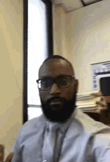 a man with glasses and a beard is taking a selfie in front of a window