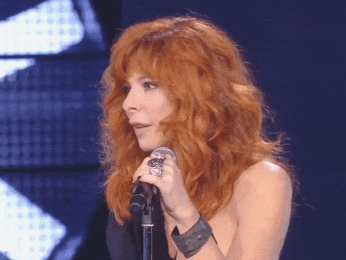 a woman with red hair singing into a microphone with a ring on her finger