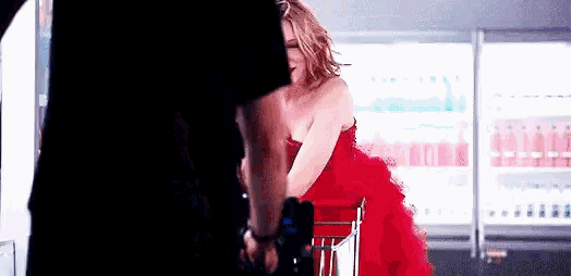 a woman in a red dress is standing next to a man holding a gun in a store .
