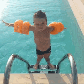a young boy wearing arm floats is standing on a ladder in a swimming pool