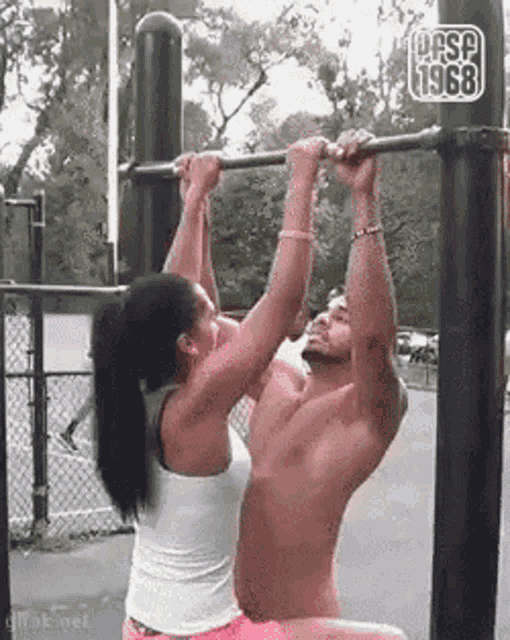 a woman is helping a shirtless man do a pull up .