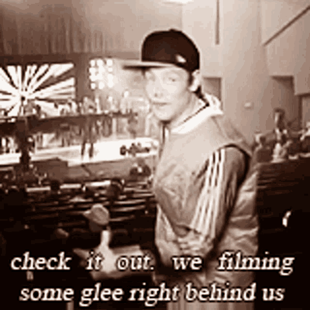 a black and white photo of a man in a baseball cap with the words check it out we filming some glee right behind us below him