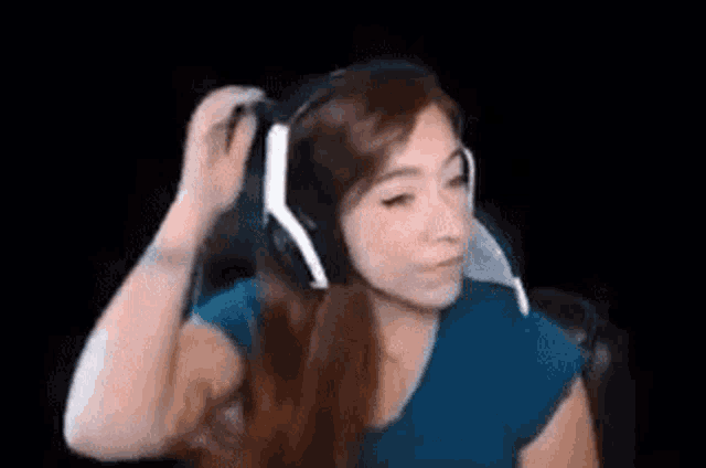 a woman wearing headphones and a blue shirt is sitting in a chair in front of a black background .