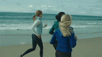 a woman in a blue jacket is running on a beach