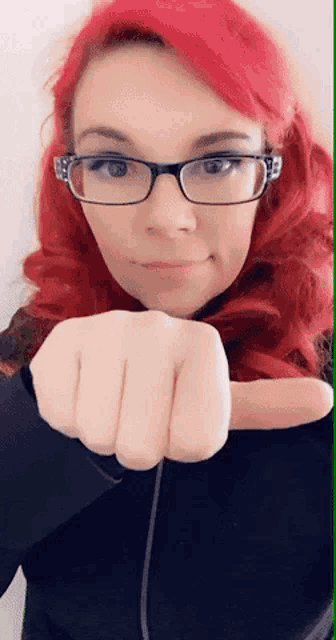 a woman with red hair and glasses holds her fist up